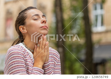 Caucasian young woman praying with closed eyes to God asking for blessing help forgiveness outdoors Caucasian young woman praying with closed eyes to God asking for blessing help forgiveness outdoors 128656749