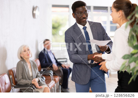Woman makes deal, shaking hands with middle-aged African man colleague while standing in office 128656826