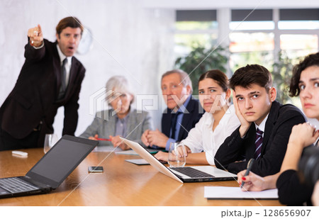 Frustrated guy sitting in office with coworkers and irritated boss 128656907