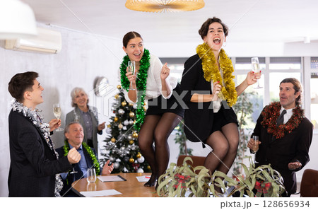 Cheerful young women dancing on table during Christmas party in office 128656934