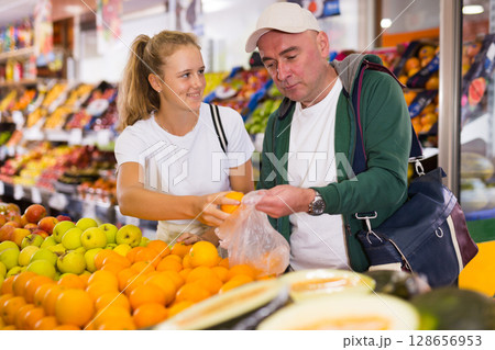 Man with a fifteen-year-old girl choose oranges at the counter 128656953
