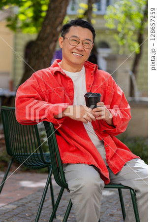 Happy Asian man enjoying drinking morning coffee hot drink, relaxing, taking a break on city street 128657259