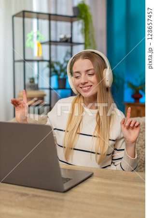 Caucasian woman listening to calming music, working on laptop at home on table, smiling, relaxed 128657457