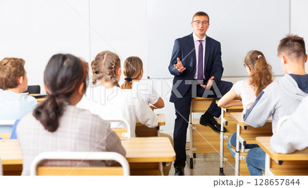 Man teacher with notebook is giving interesting lecture for students in classroom 128657844