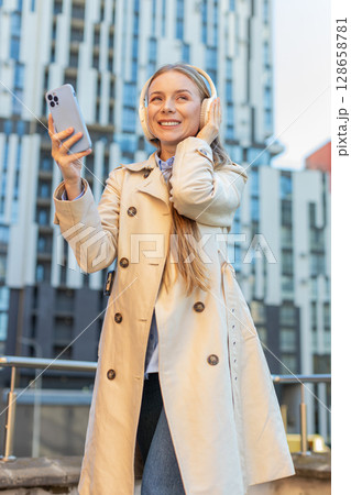 Happy mature businesswoman in headphones listening favorite energetic music on smartphone on street 128658781