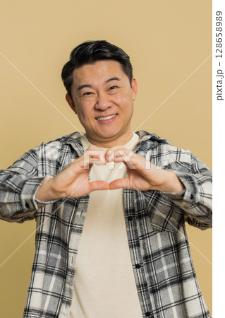 Happy Asian man makes heart gesture demonstrates love sign expresses good feelings and sympathy 128658989