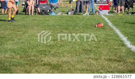 Youth football game held in a sunny park with spectators and a scoreboard in the background Youth football game held in a sunny park with spectators and a scoreboard in the background 128661577