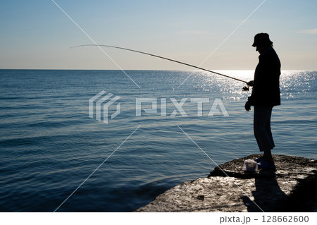 silhouette of a fisherman catches fish at sea 128662600