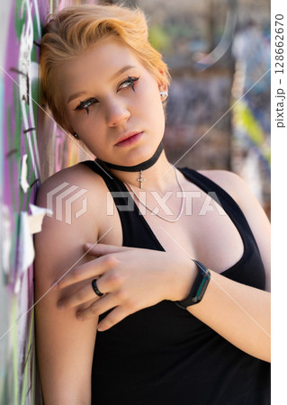 a fashionable girl with a bright short hairstyle and candid makeup poses against the background of a graffiti wall. 128662670