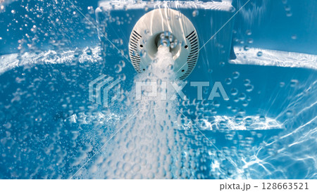 Close-up underwater view of a pool jet releasing bubbles with intense pressure, surrounded by blue water and light reflections. Close-up underwater view of a pool jet releasing bubbles with intense pressure, surrounded by blue water and light reflections. 128663521