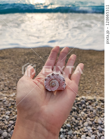 holding a seashell in his hand with a view of the sea and the beach 128665311
