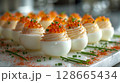 Caviar Deviled Eggs float elegantly, showcasing creamy yolk filling, caviar, chives, and paprika, emphasizing their luxurious and gourmet appeal. 128665434