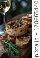 Foie gras with a glass ampoule of white wine and rosemary jelly served on a rustic wooden board, accompanied by a sprig of fresh rosemary and a small side of toasted brioche 128665440