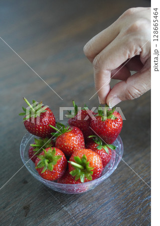Hands are picking strawberries. Many fresh strawberries in a clear plastic glass lid on a wooden table background, fruit, food, decor, object, copy space Hands are picking strawberries. Many fresh strawberries in a clear plastic glass lid on a wooden table background, fruit, food, decor, object, copy space 128665464
