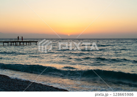 silhouette of people walking along the sea beach pier at sunset 128665986