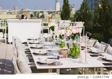 Exquisitely set long dining table on a sunlit rooftop terrace Exquisitely set long dining table on a sunlit rooftop terrace 128667796