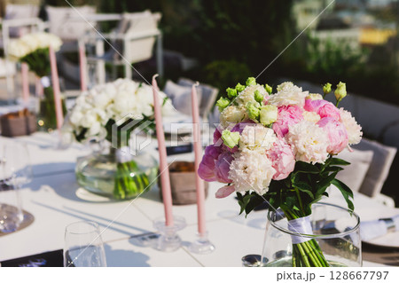An elegant outdoor table setting adorned with beautiful bouquets of pink and white peonies 128667797