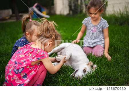 Joyful children playing with a friendly dog in a sunny garden Joyful children playing with a friendly dog in a sunny garden 128670480