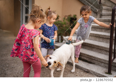 Joyful children playing and grooming a dog in a sunny garden 128670502