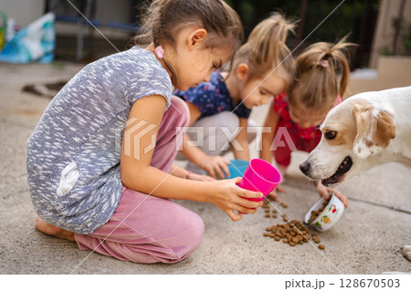 Children joyfully share snacks with a friendly dog in the backyard Children joyfully share snacks with a friendly dog in the backyard 128670503
