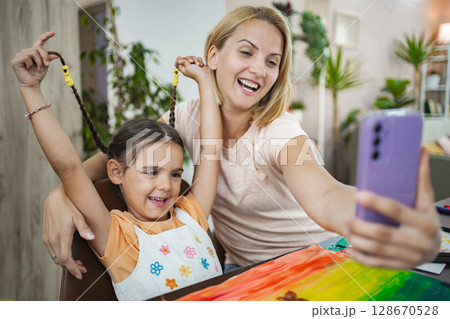 Mother and daughter enjoy a creative art session at home, capturing a joyful selfie Mother and daughter enjoy a creative art session at home, capturing a joyful selfie 128670528