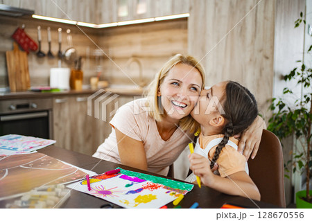 Cute girl kisses her mother while they both work on vibrant art projects 128670556