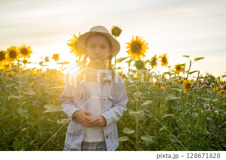A young girl stands amidst a vibrant sunflower field during the stunning sunset hour A young girl stands amidst a vibrant sunflower field during the stunning sunset hour 128671828