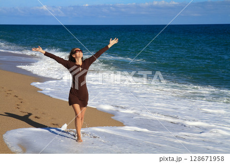 a beautiful girl in a brown dress is walking on the sandy beach and enjoying the sea view a beautiful girl in a brown dress is walking on the sandy beach and enjoying the sea view 128671958