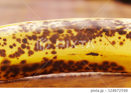 A ripe banana with dark brown spots lies on a wooden surface in a kitchen 128672598