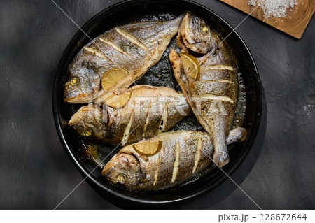 Juicy dorado fish is carefully grilled to perfection, garnished with lemon slices and herbs Juicy dorado fish is carefully grilled to perfection, garnished with lemon slices and herbs 128672644
