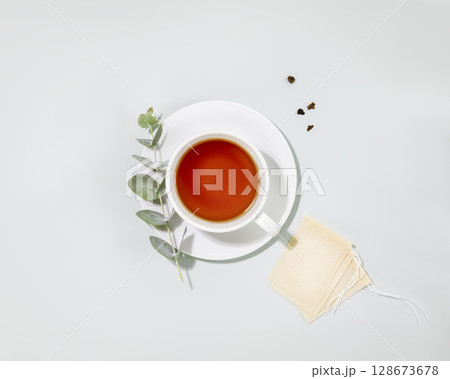 Cup of tea. Eco friendly still life with cup of tea, eucalyptus sprig and paper tea bags on blue background. Concept of organic tea and healthy natural drink. Flat lay 128673678