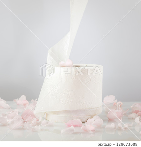 Roll of natural white toilet paper on a light background with rose petals. White toilet tissue, Hygiene product. Restroom soft touch toilet paper. Soft focus style image. Front view 128673689