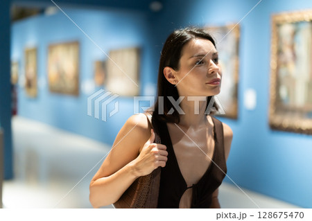 Young woman in summer clothes looking at paintings in museum 128675470