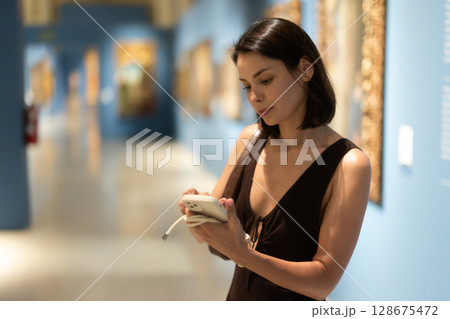 While visiting museum, girl uses travel guide application on her phone. While visiting museum, girl uses travel guide application on her phone. 128675472