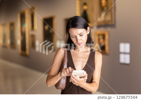 While visiting museum, girl uses travel guide application on her phone. 128675504