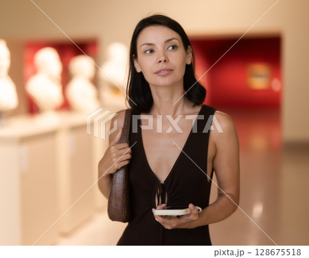 Woman with phone in hands in museum hall, view statues exhibition. Woman with phone in hands in museum hall, view statues exhibition. 128675518