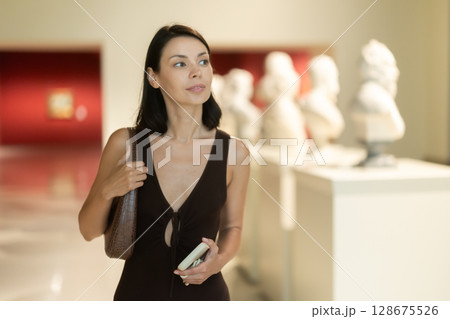 Woman with phone in hands in museum hall, view statues exhibition. Woman with phone in hands in museum hall, view statues exhibition. 128675526