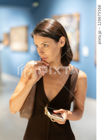 Woman with phone in hands in museum hall, view painting exhibition 128675566