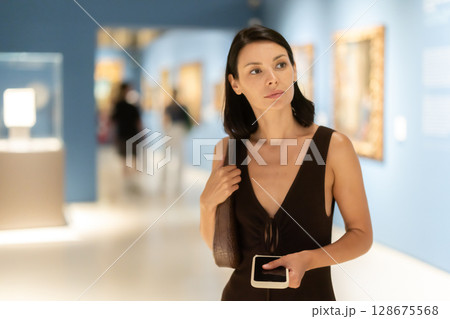 Young woman in summer clothes looking at paintings in museum Young woman in summer clothes looking at paintings in museum 128675568