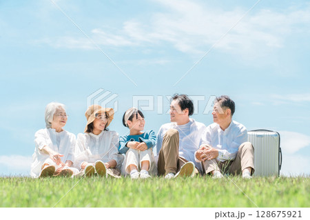 青空の見える公園・丘に座る家族・親子・三世代家族（父親・母親・娘・祖母・祖父） 128675921