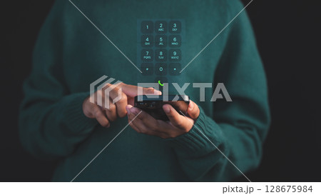 Person dialing on a smartphone with a futuristic virtual keypad interface hovering, symbolizing advanced communication. Concept of digital security and data protection on mobile devices. 128675984