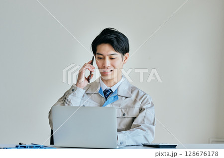 電話をする作業服姿の若い男性 電話をする作業服姿の若い男性 128676178