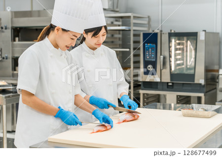魚を調理するコックコート姿の女性スタッフ（調理師・専門学校・料理人・生鮮市場・食品加工） 128677499
