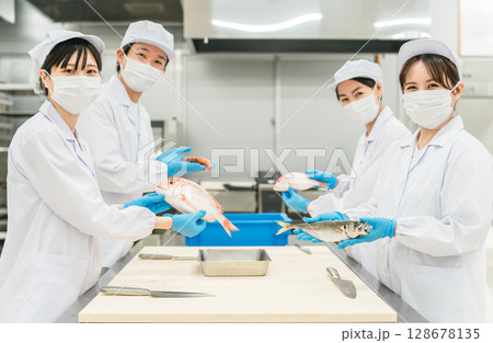 魚を調理するコックコート姿の男女スタッフ(調理師・料理人・生鮮市場・食品加工) 魚を調理するコックコート姿の男女スタッフ(調理師・料理人・生鮮市場・食品加工) 128678135