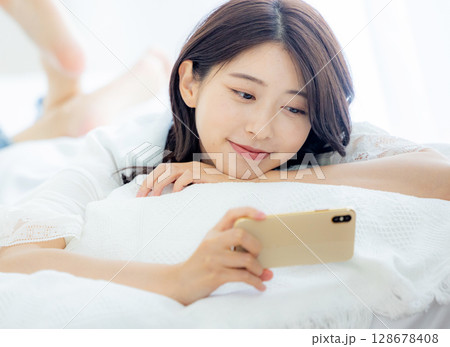 ベッドでスマホを見る女性 128678408