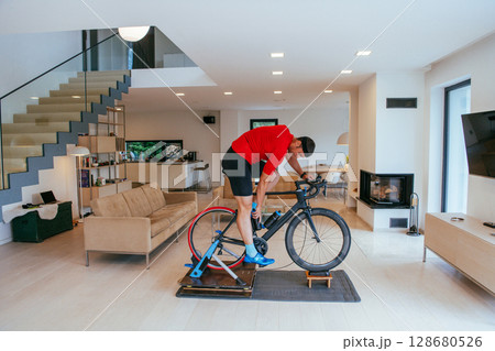 A triathlete riding a triathlon bike on a machine simulation in a modern living room 128680526