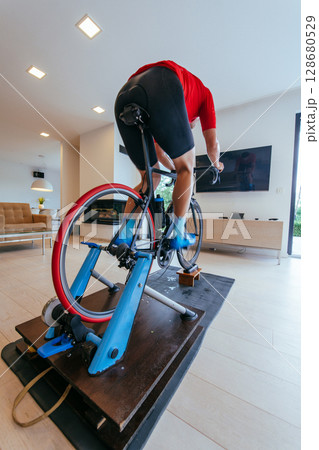 A triathlete riding a triathlon bike on a machine simulation in a modern living room A triathlete riding a triathlon bike on a machine simulation in a modern living room 128680529