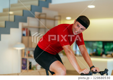 A triathlete riding a triathlon bike on a machine simulation in a modern living room A triathlete riding a triathlon bike on a machine simulation in a modern living room 128680530