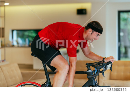 A triathlete riding a triathlon bike on a machine simulation in a modern living room 128680553