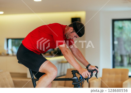 A triathlete riding a triathlon bike on a machine simulation in a modern living room 128680556